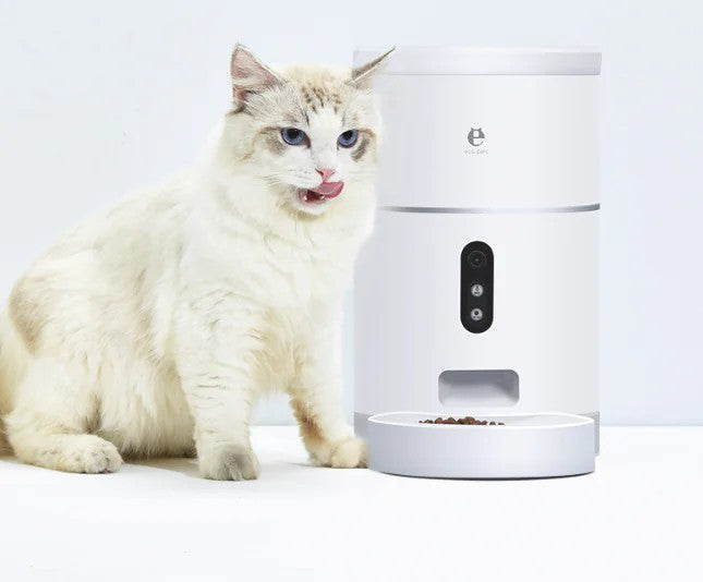 White automatic WiFi pet feeder beside a cat, food in the bowl and camera lens visible