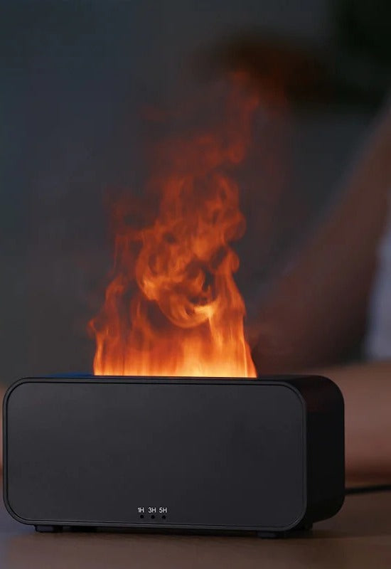 Black flame effect aromatherapy diffuser glowing with a realistic orange flame of backlit mist, 1H/3H/5H timer buttons visible on the front, in a dim bedroom.