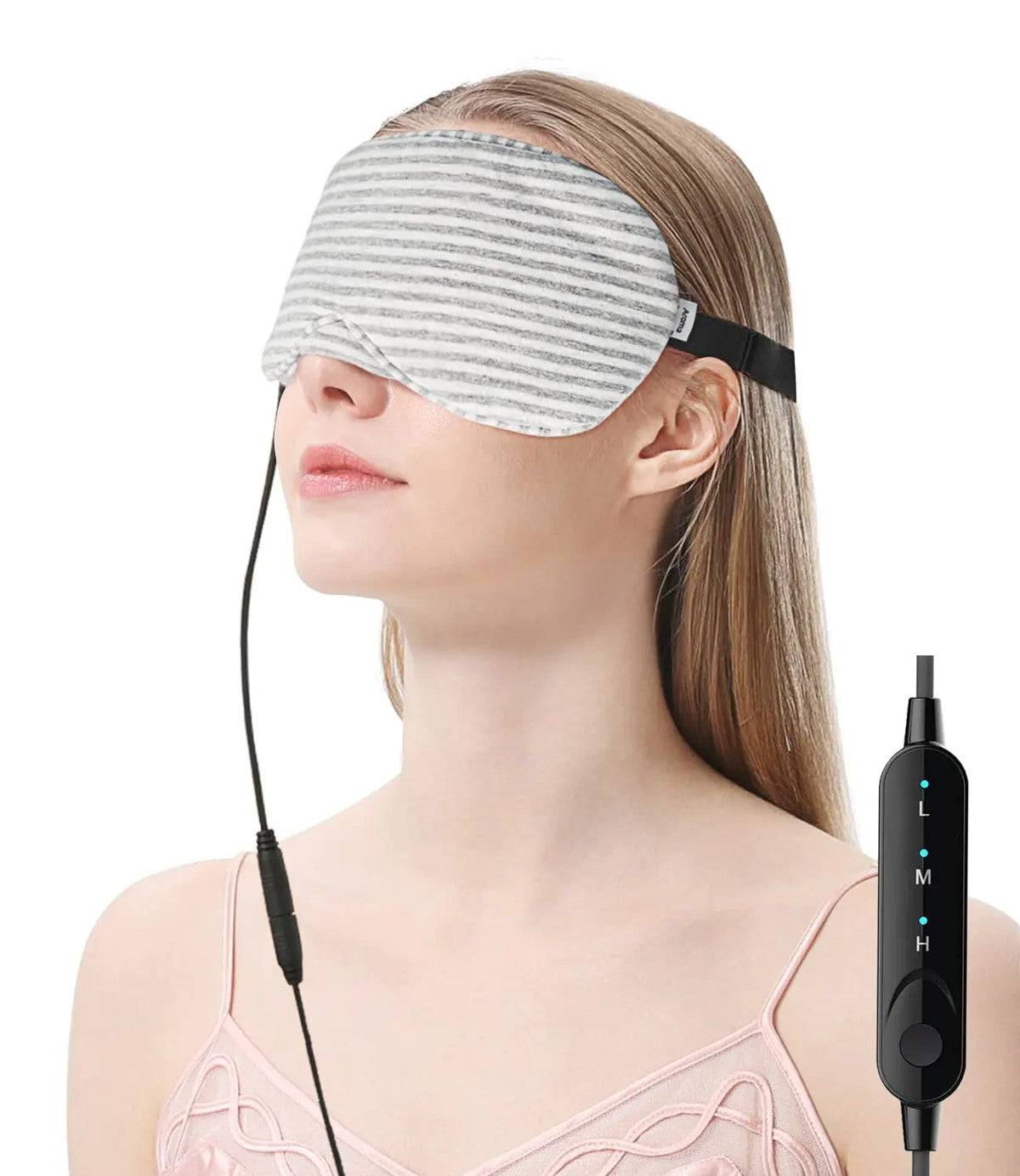 Woman relaxing with a soft grey-and-white striped 100% cotton USB heated eye mask over her closed eyes, the cord running to an inline Low/Med/High warmth controller — a plug-in warm compress for screen-tired eyes.