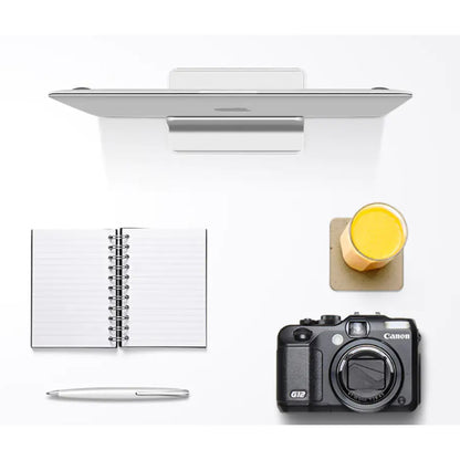 Overhead desk setup with the laptop stored upright in the stand beside a notebook and camera