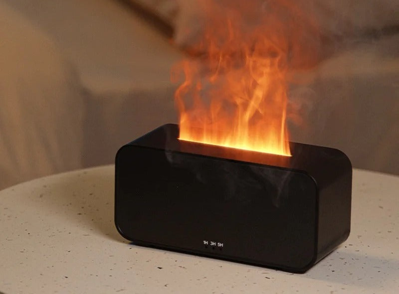 Black flame diffuser on a nightstand releasing a soft flame-lit mist column with a made bed in the background, 1/3/5-hour timer controls on the front.